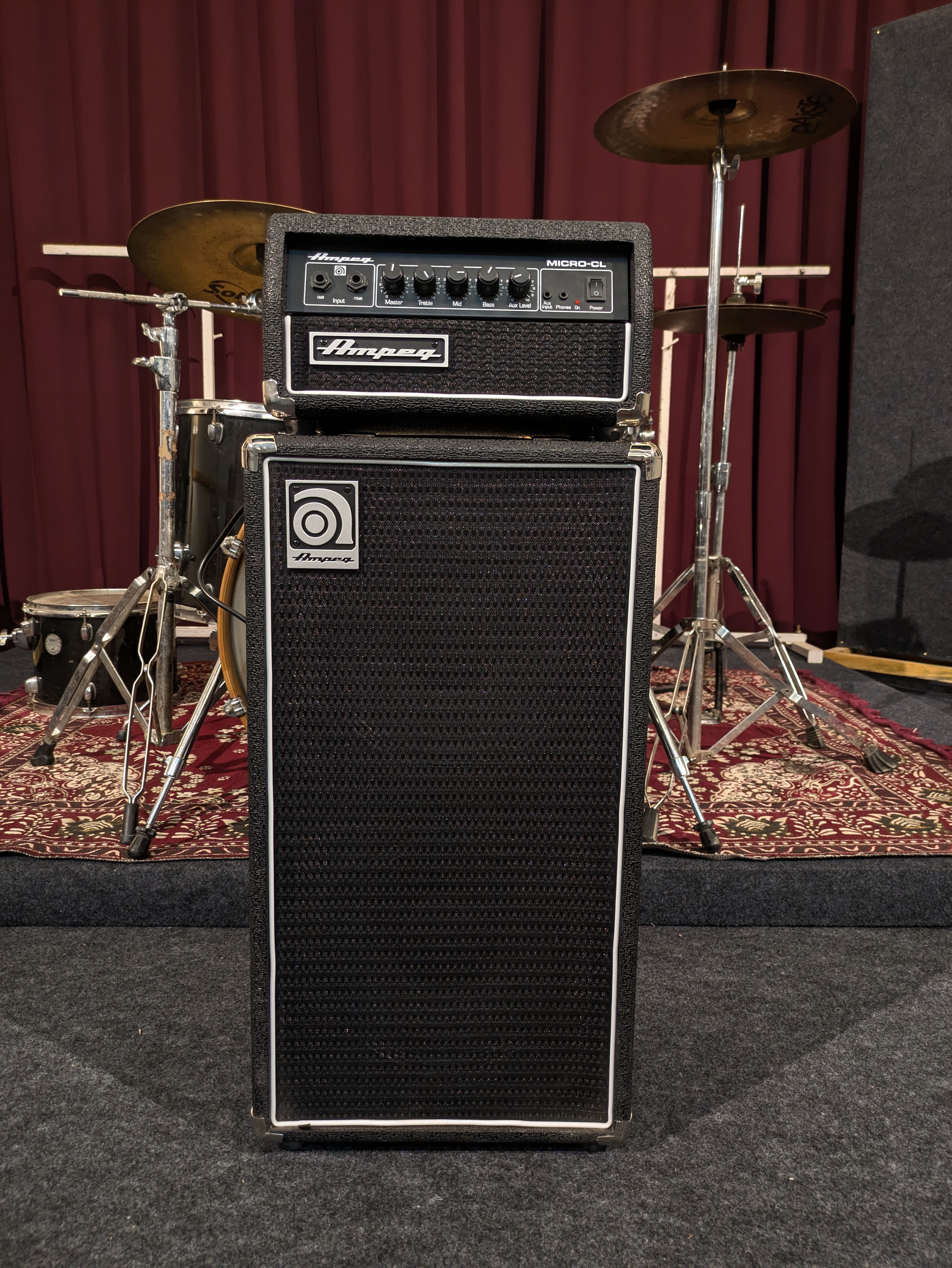 Bass amplifier head on its cabinet, on the stage in front of the drum kit